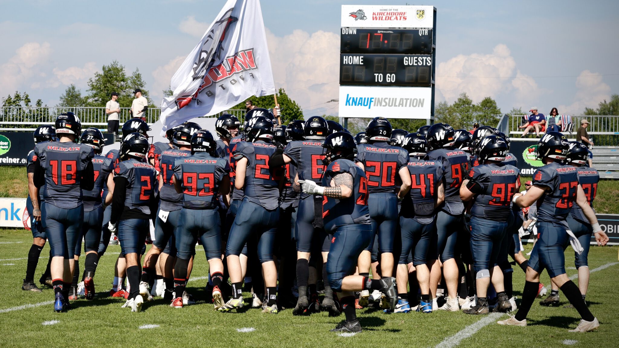 Die Kirchdorf Wildcats stehen mit ihrer Vereinsfahne im Teamkreis auf dem heimischen Spielfeld